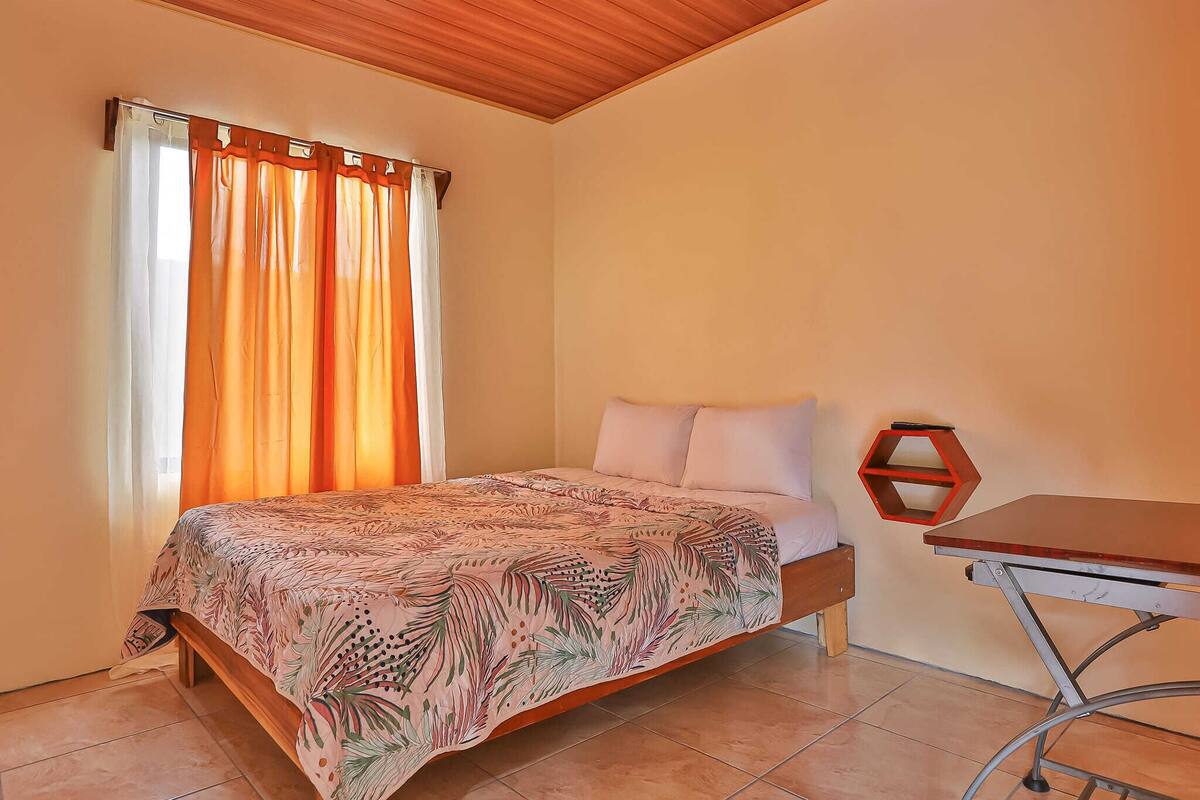 A bedroom with a bed, a table, and curtains.