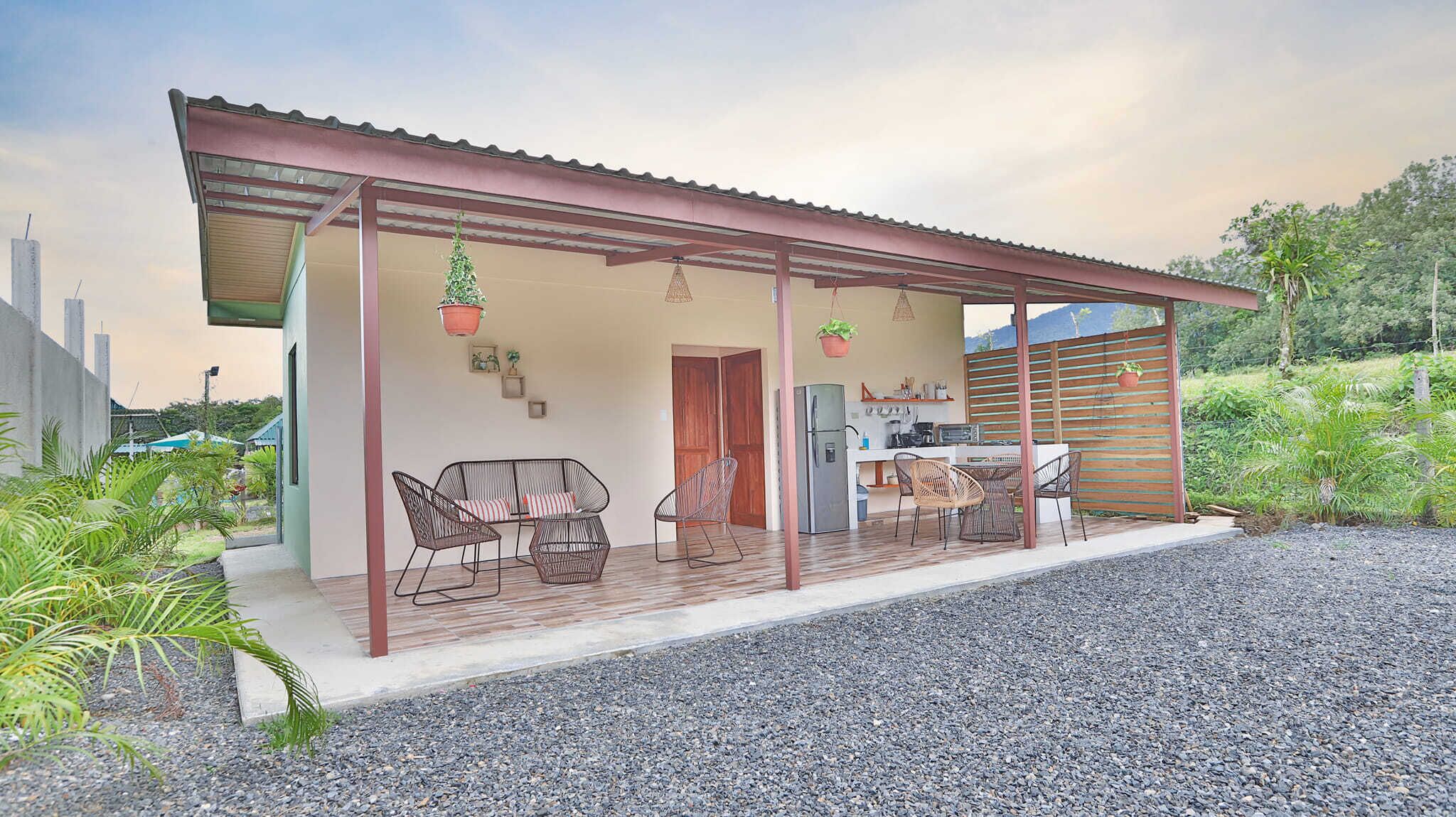 Una casa con porche cubierto, mobiliario exterior y espacio para la cocina.
