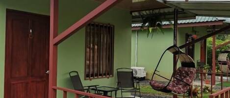 A house with a porch, a swing chair, a table, and potted plants.
