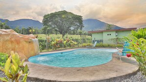 Une piscine agrémentée d’une cascade, entourée de plantes tropicales et avec une chaîne de montagnes en toile de fond.