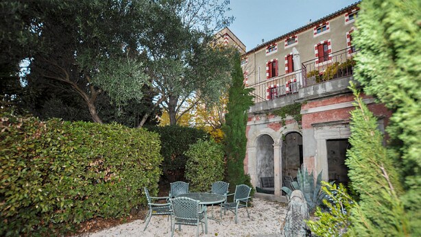 A courtyard with a table and chairs, surrounded by hedges and trees.