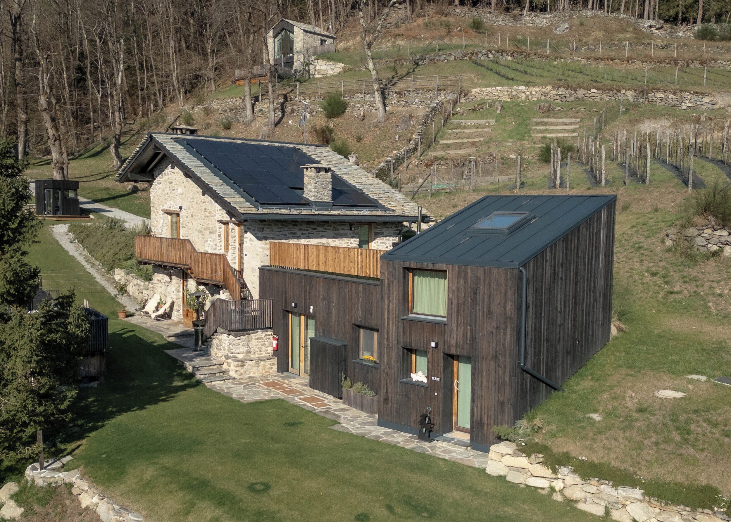 Et moderne hus med en stenfacade, en træterrasse og et stort mørkt tag.