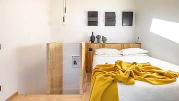 Een moderne slaapkamer met een houten hoofdbord, een bed met wit beddengoed en een gele plaid, en een klein nachtkastje met decoratieve objecten.