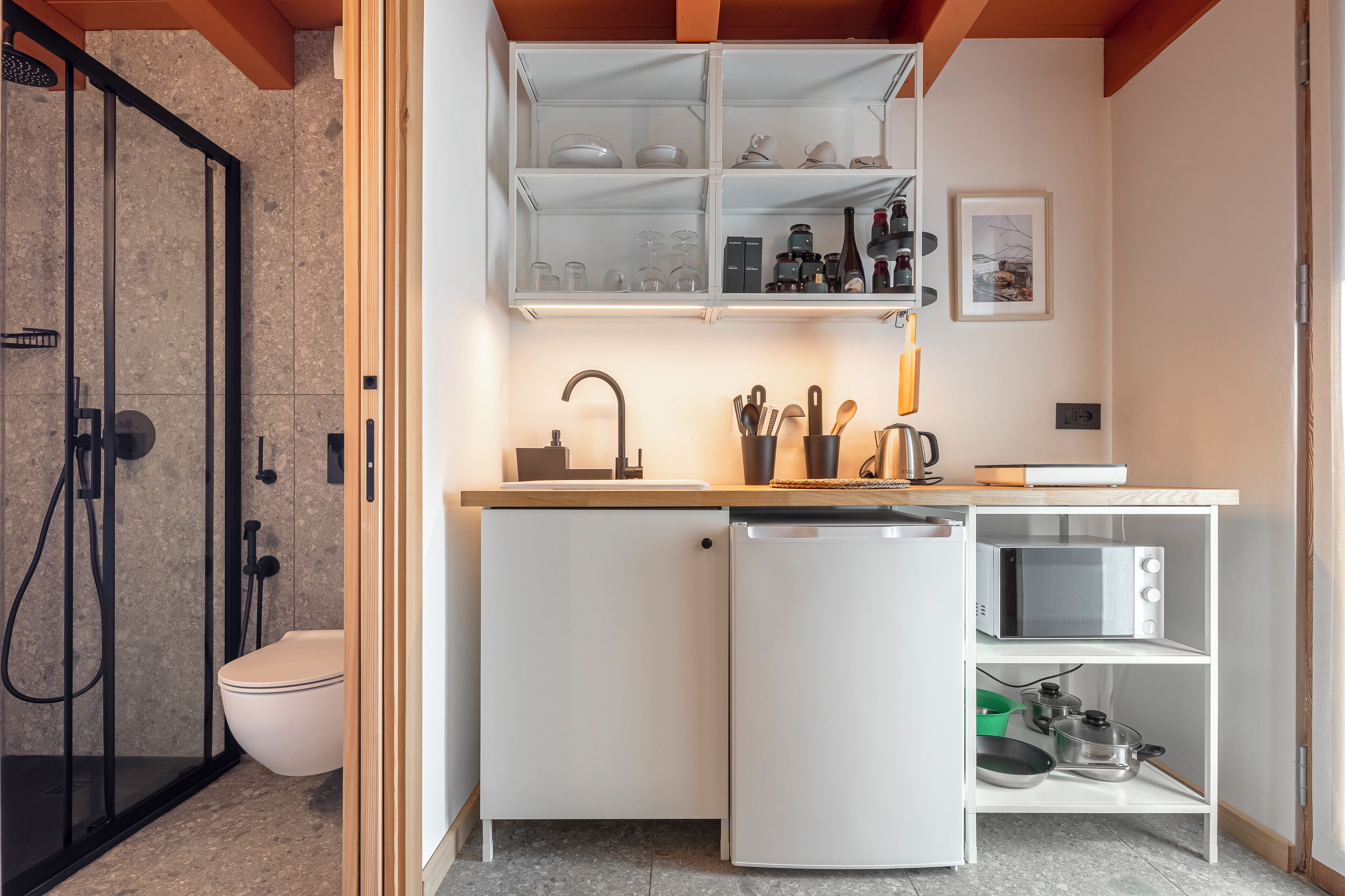 A compact kitchen with a dishwasher, microwave, and open shelving with dishes and utensils.