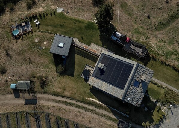 Vista aérea de una propiedad que incluye un edificio grande con techo solar, una construcción más pequeña contigua y un área cercada con mobiliario exterior.