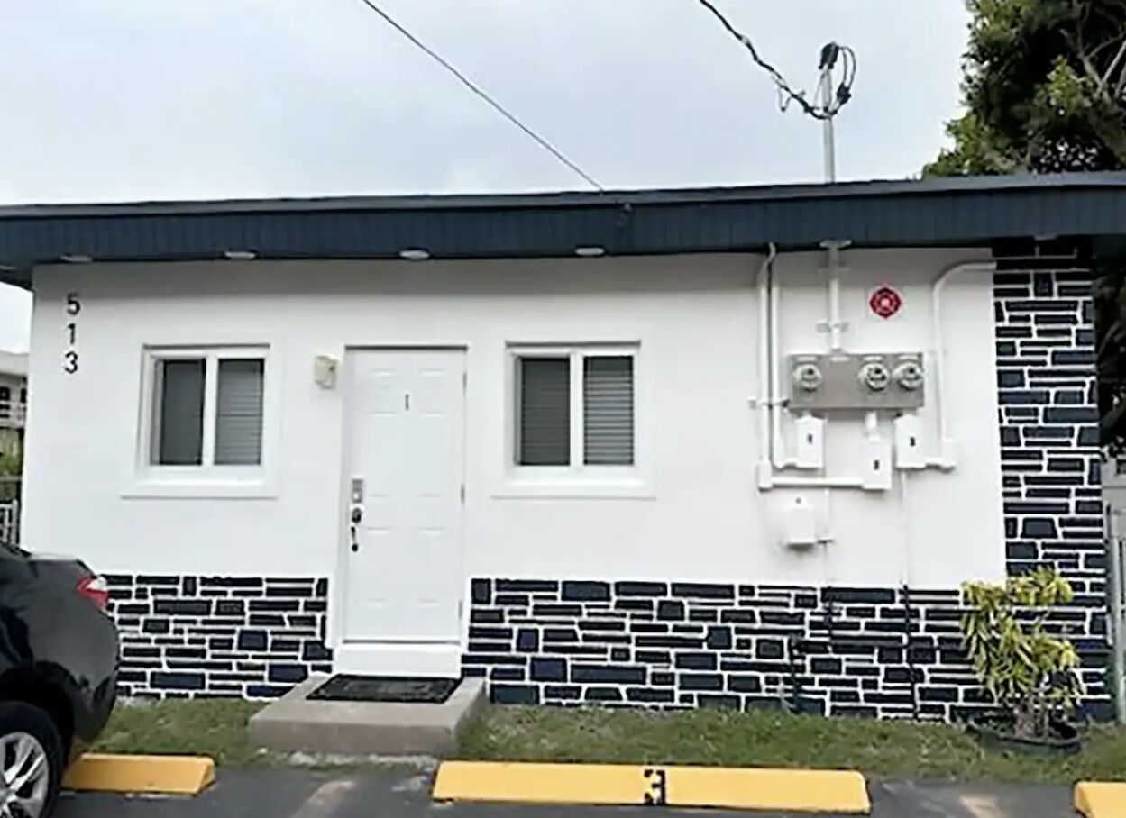 A single-story building with a white exterior, two windows, a door, and a small porch.