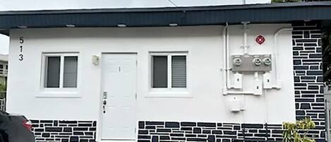 A single-story building with a white exterior, two windows, a door, and a small porch.