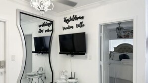 Une chambre à coucher avec un lit, une télévision, un miroir et un panneau décoratif au mur.