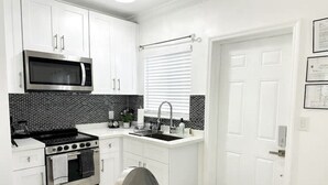 Une cuisine moderne avec des meubles blancs, une cuisinière en acier inoxydable, un four à micro-ondes et un évier placé sous une fenêtre.