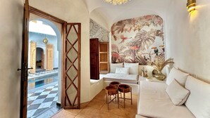 A spacious room with a large bed, a sofa, and a dining area. There is a decorative wall with a tropical mural and a chandelier. - Riad LallaBaya (Marrakech)