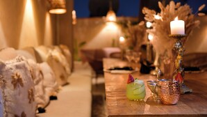 A cozy dining area with a wooden table, candles, and a candle holder with a lit candle. There are two drinks on the table, one with a straw and a slice of fruit. - Riad LallaBaya (Marrakech)