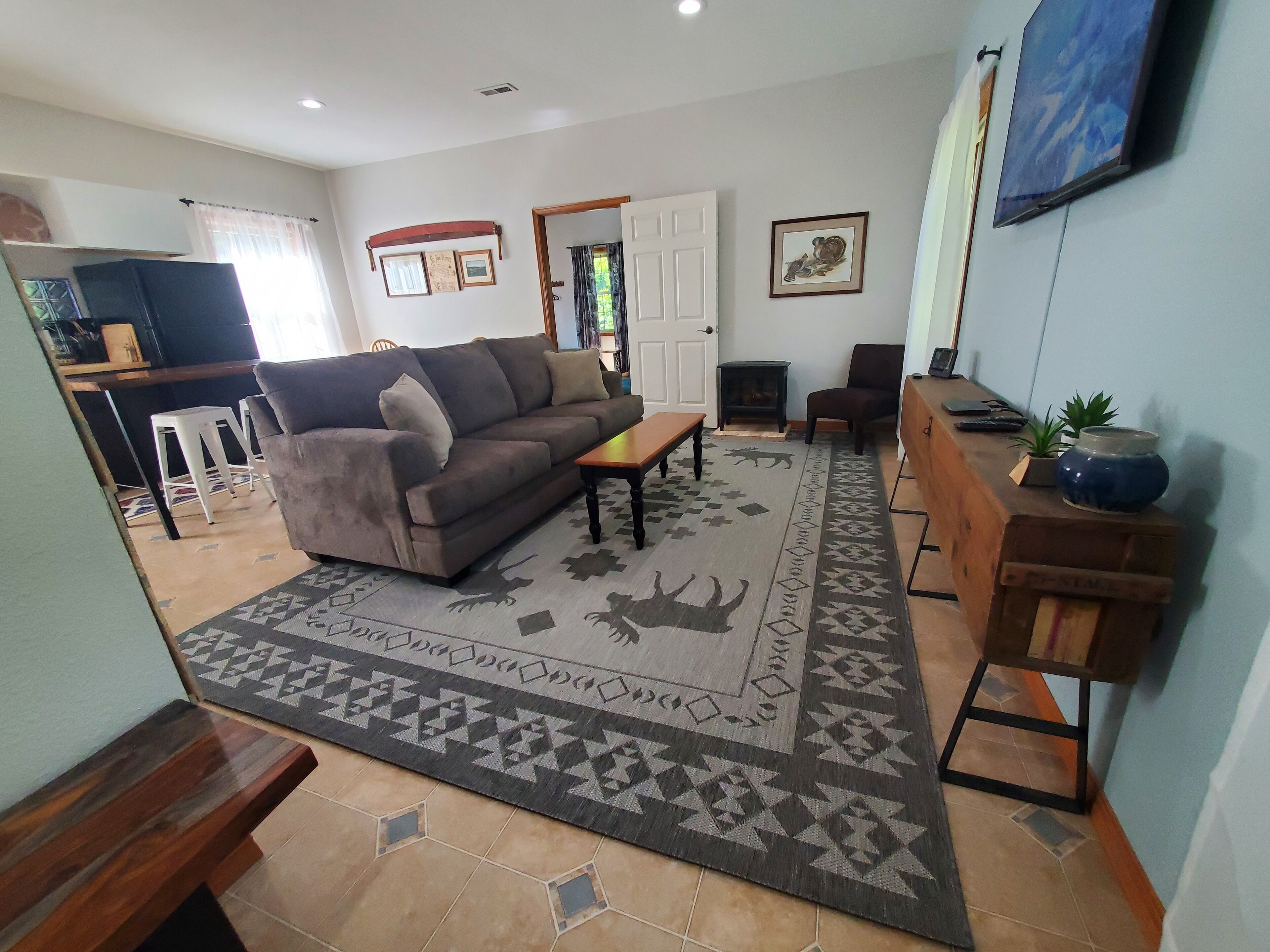 Un salon avec un canapé, une table basse, un tapis et un téléviseur fixé au mur.