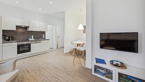 A modern kitchen with white cabinets, a dining area with a table and chairs, and a mounted flat-screen TV.