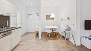 A modern kitchen with white cabinets and a built-in oven, a dining area with a white table and chairs, a small bench, and a radiator.