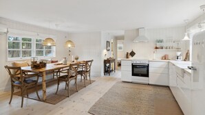 A spacious kitchen with white cabinetry, a dining area with wooden furniture, and a view of the outdoors through large windows.
