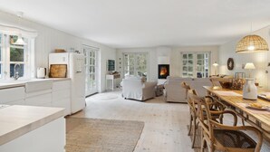 A spacious kitchen with white cabinetry, a dining area with wooden furniture, and large windows allowing natural light.