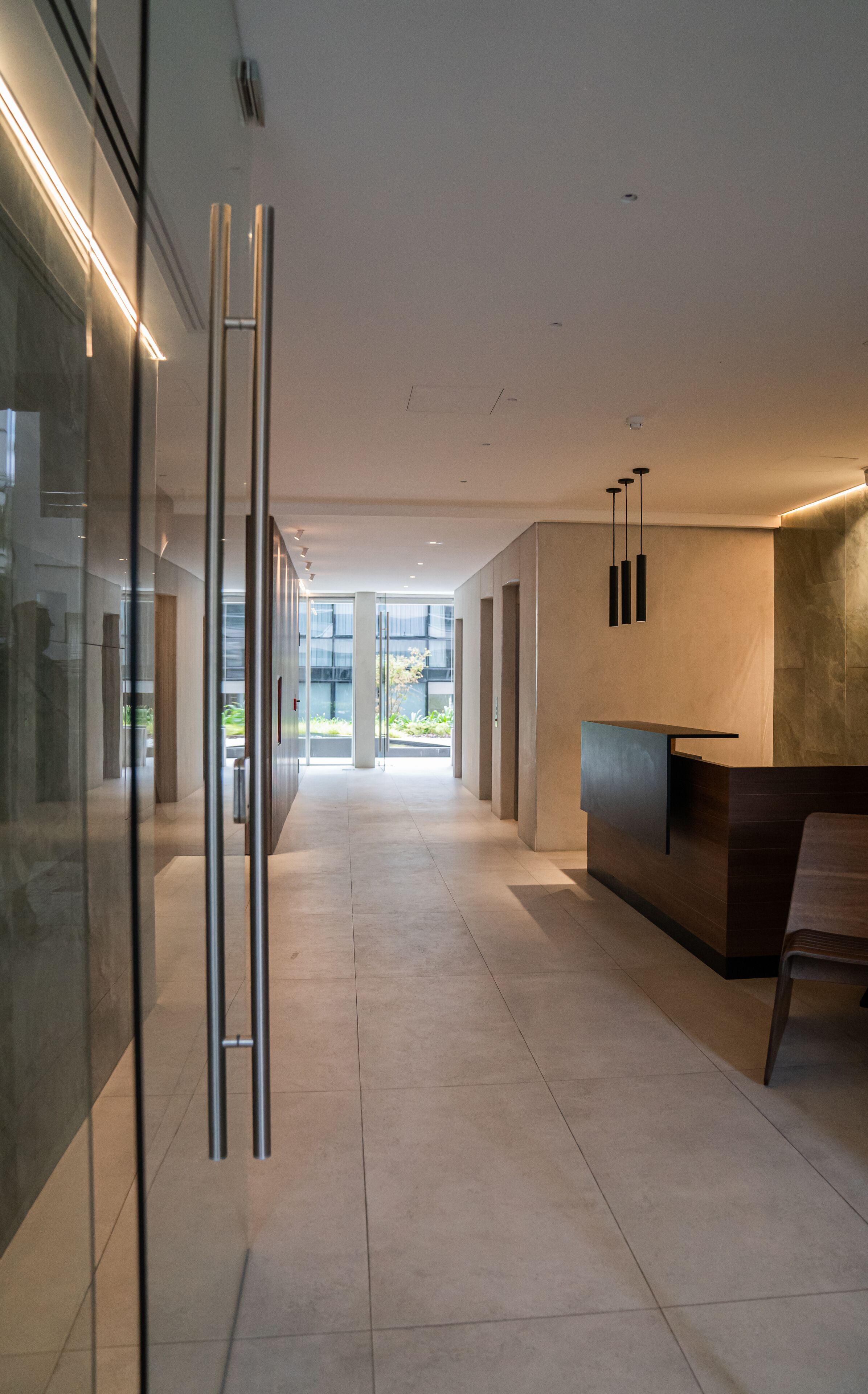 A modern reception area with a glass partition, a reception desk, and a view of the outdoors.