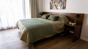 A bedroom with a wooden bed, a nightstand, a wall-mounted lamp, and a geometric artwork.