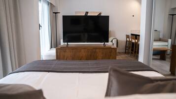 Habitación de hotel con una cama grande, un televisor sobre un soporte de madera, un escritorio con sillas y un sofá.