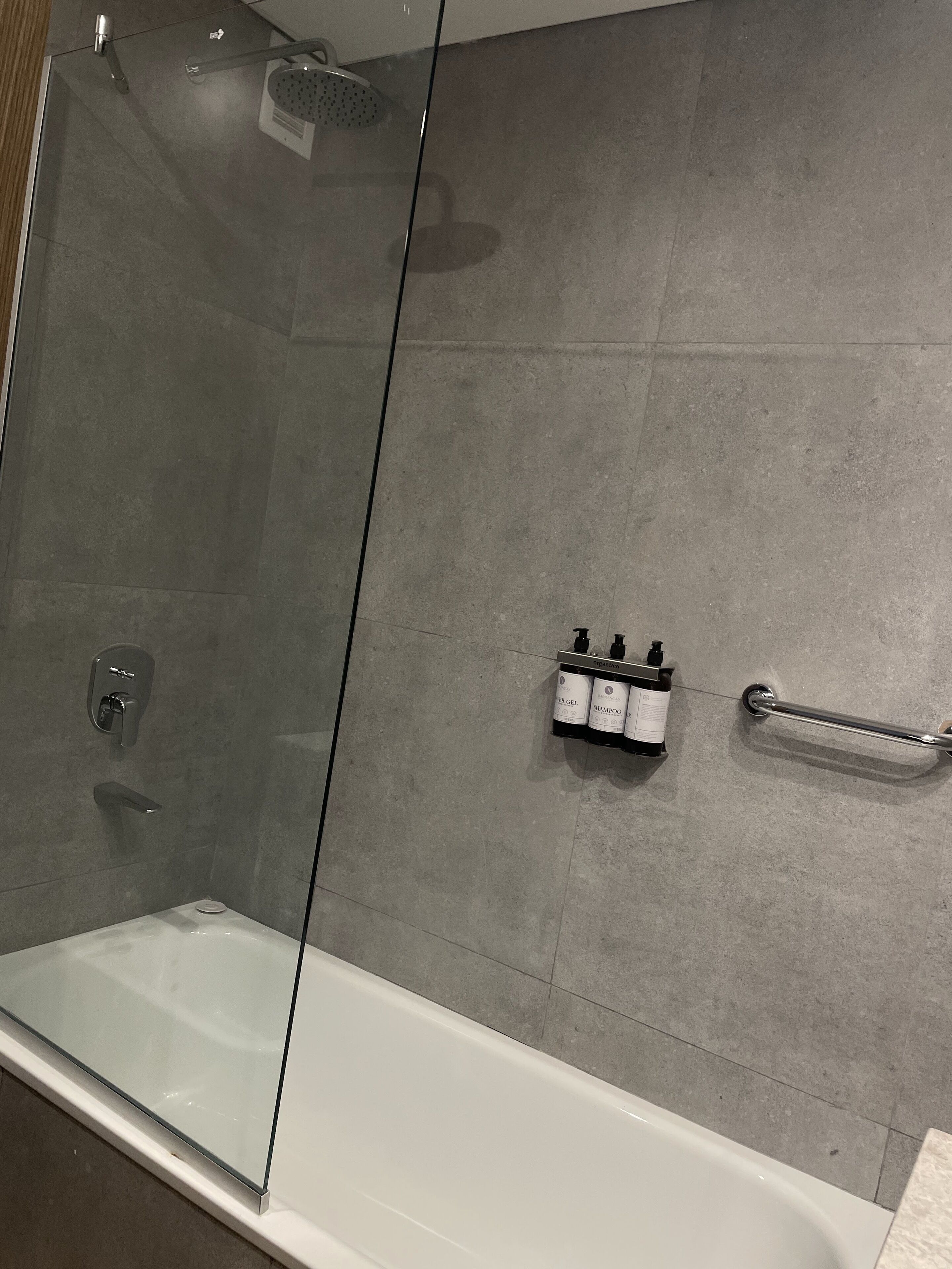 A modern bathroom with a glass-enclosed shower, a white bathtub, and a wall-mounted shampoo and conditioner dispenser.