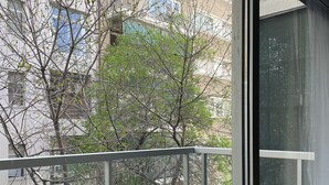 A balcony with a metal railing, a view of buildings and trees, and a window with a view of the sky. - Barrancas Quality Apartments (Buenos Aires)