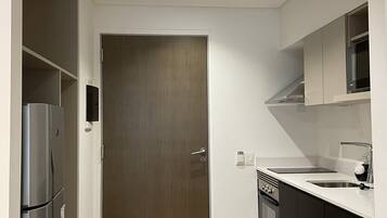A modern kitchen with a built-in oven, a stainless steel refrigerator, and a microwave. There is a wooden door and a white countertop.
