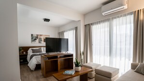 A modern hotel room with a wooden floor, a flat-screen TV, a sofa, a coffee table, and a large window with curtains. - Barrancas Quality Apartments (Buenos Aires)