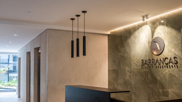 A modern reception desk with a stone wall backdrop and a logo. - Barrancas Quality Apartments (Buenos Aires)