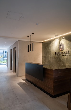 A modern reception desk with a stone wall backdrop and a logo. - Barrancas Quality Apartments (Buenos Aires)