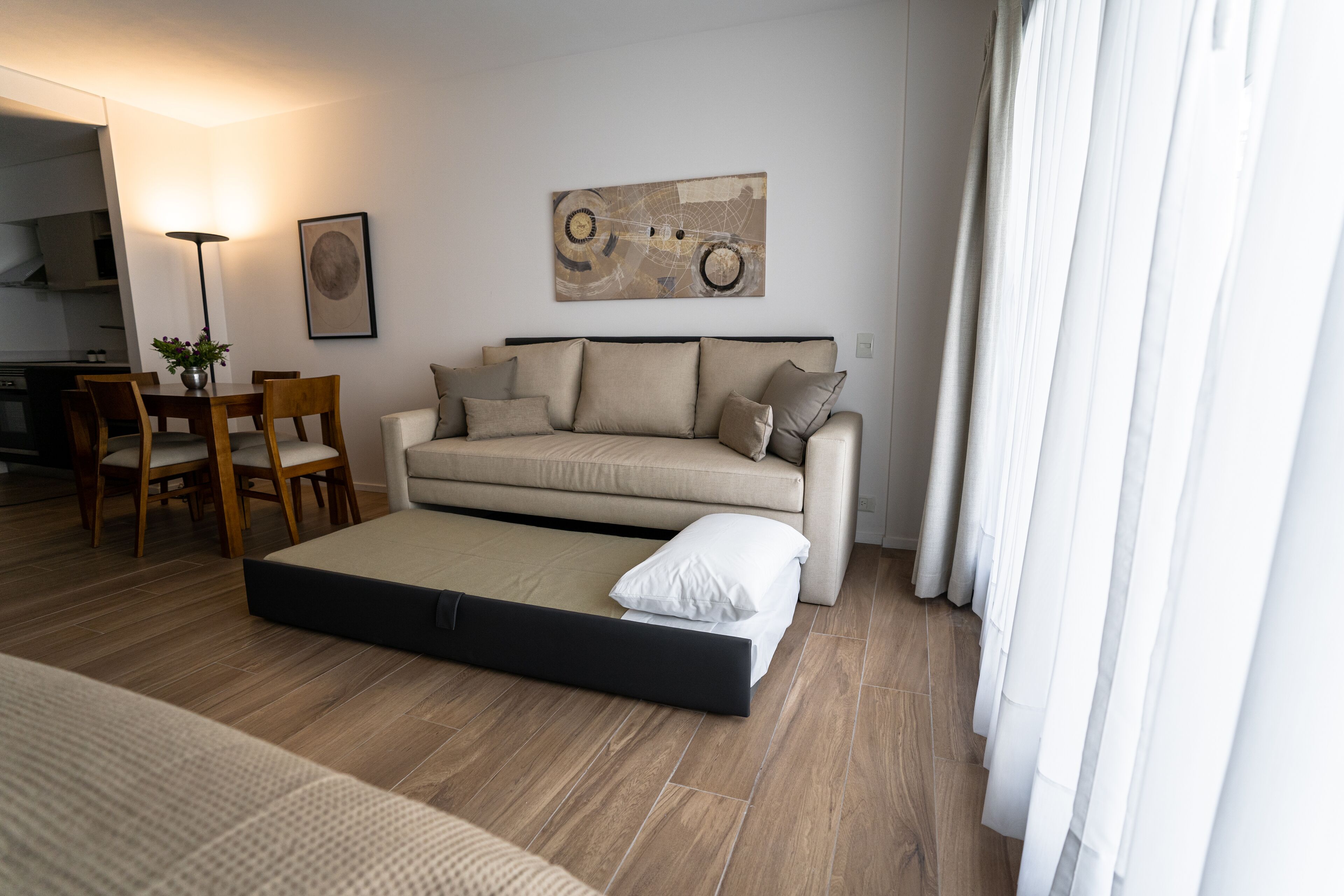 A modern living room with a sofa, a dining table with chairs, a floor lamp, and a painting on the wall.