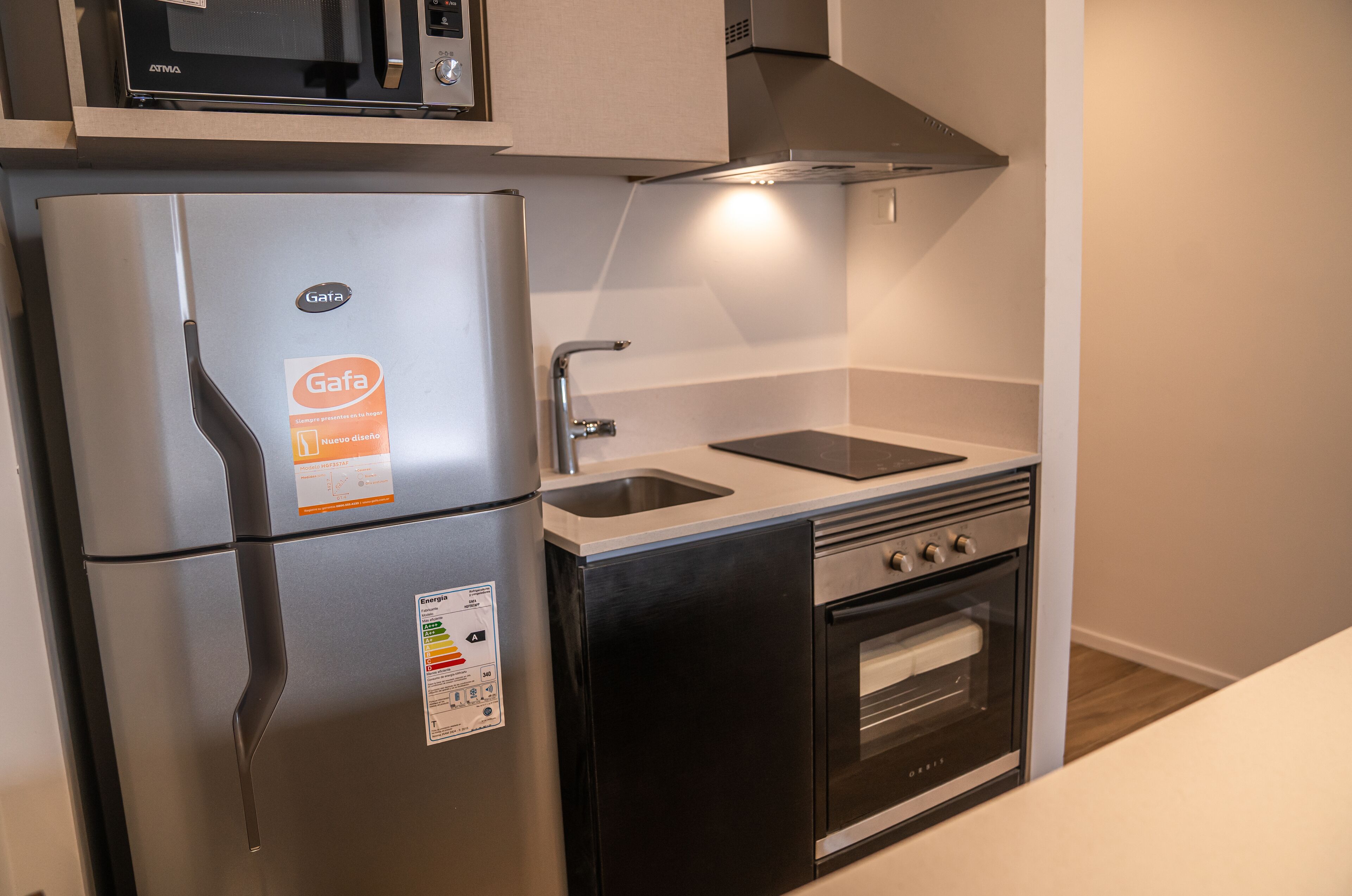 A compact kitchen with a stainless steel refrigerator, a microwave, a sink, and an oven.