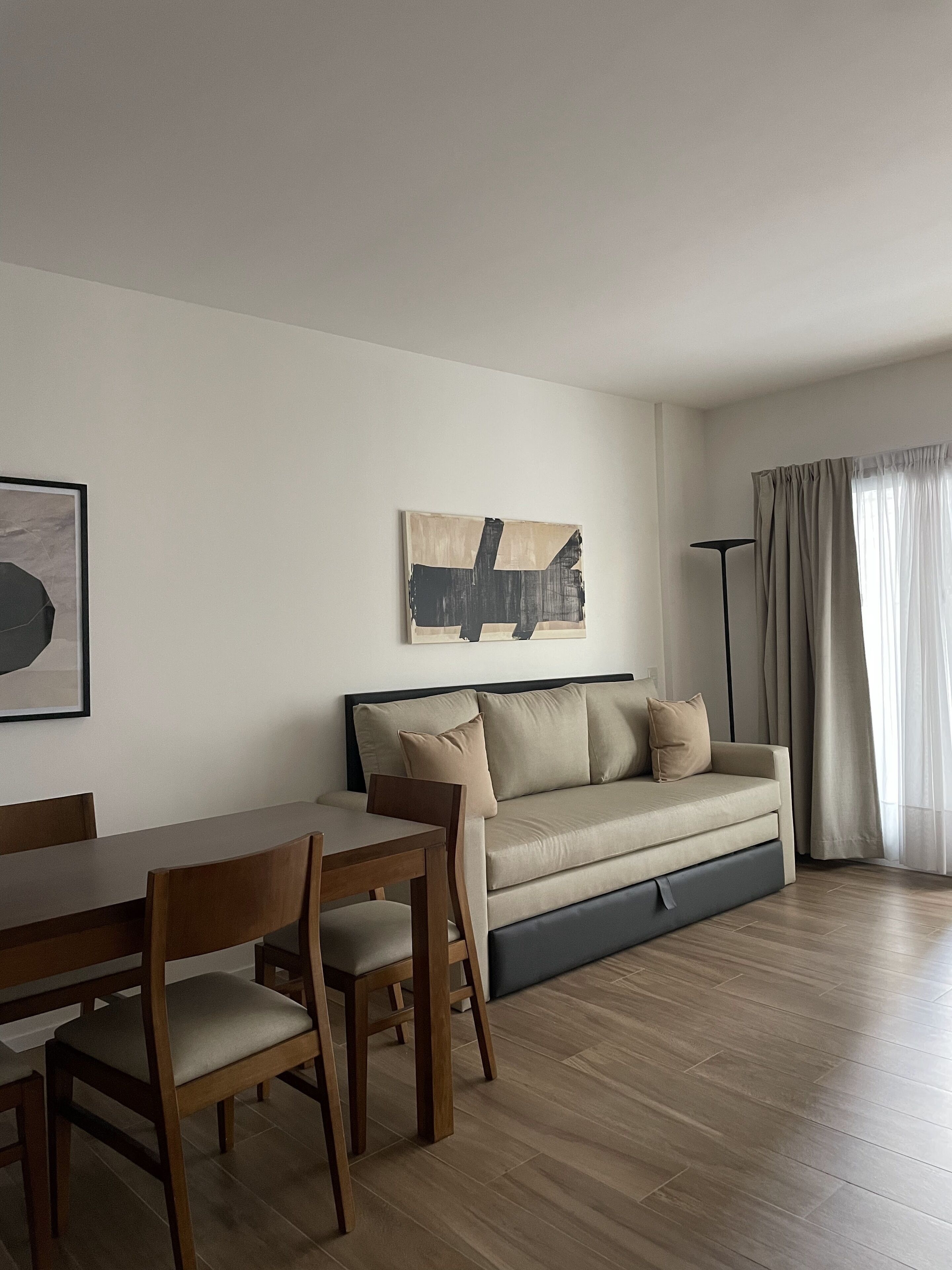 A modern living room with a sofa, a dining table with chairs, and a floor lamp.