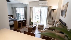 A modern living room with a sofa, coffee table, and TV. There is a balcony with curtains and a plant. - Barrancas Quality Apartments (Buenos Aires)