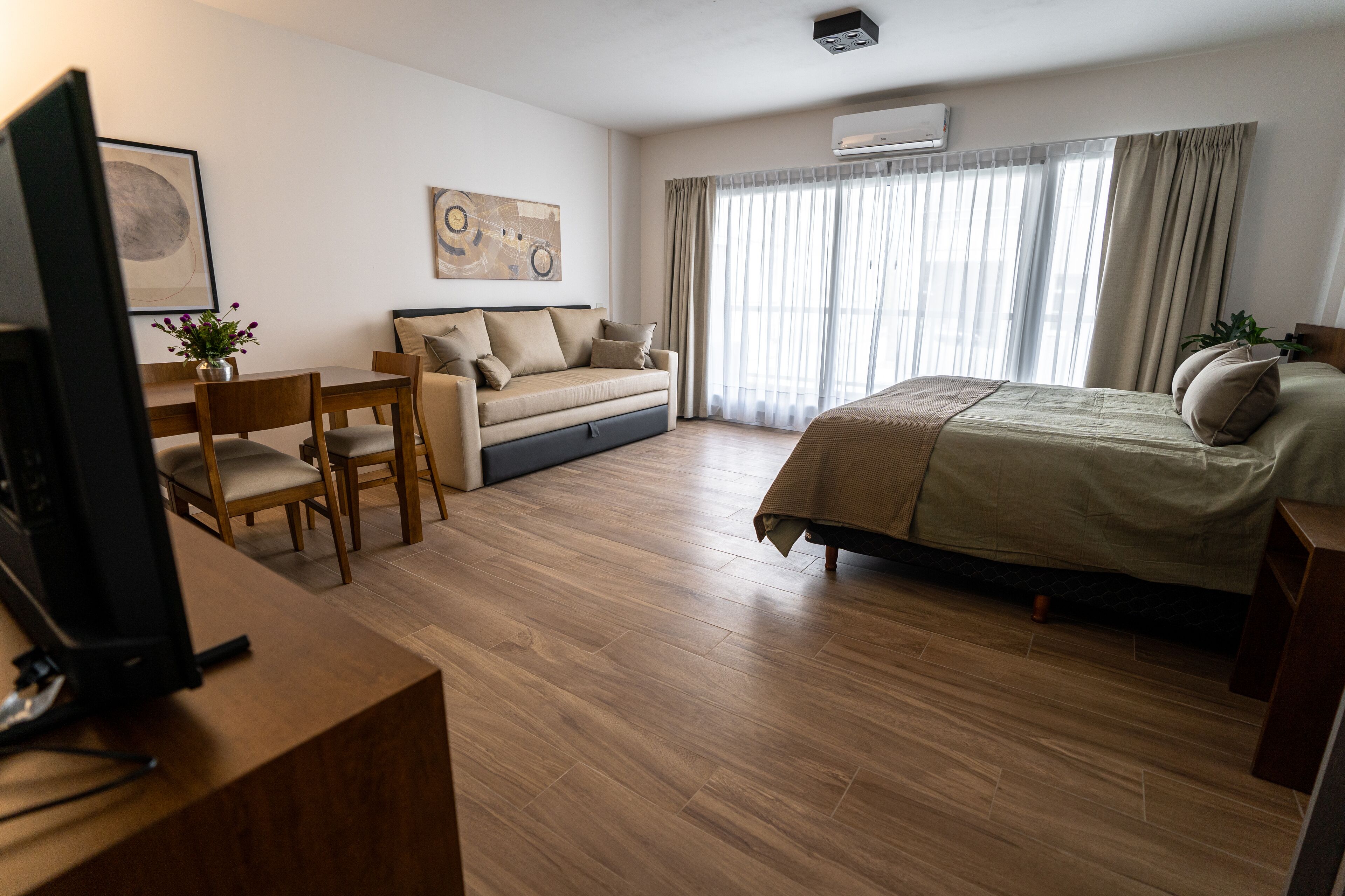A hotel room with a bed, a sofa, a desk, and a television.