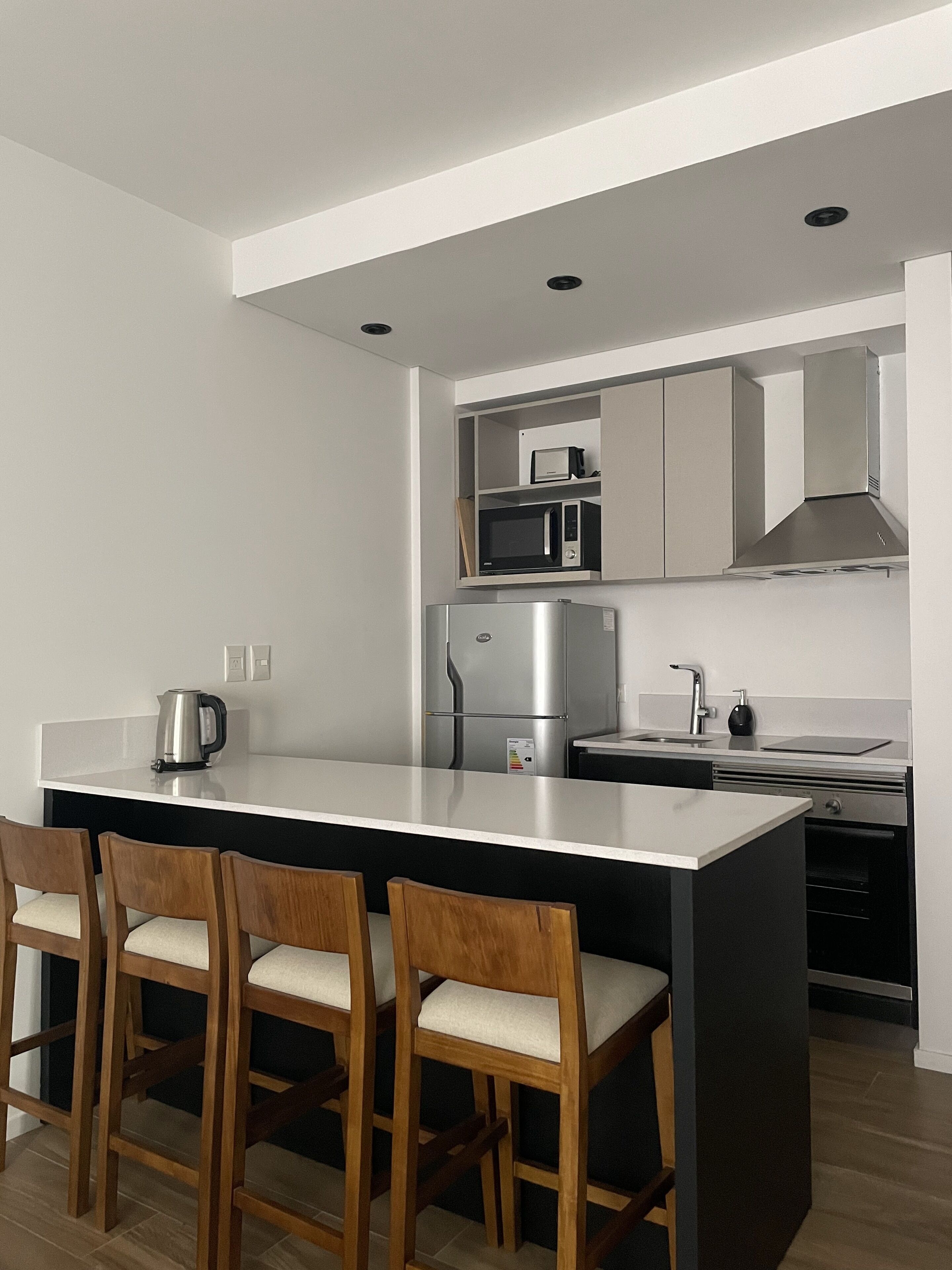 A modern kitchen with a central island, wooden bar stools, stainless steel appliances, and white cabinetry.