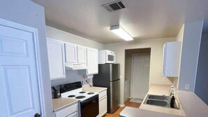 Une cuisine de taille réduite avec des meubles blancs, une cuisinière, un four à micro-ondes et un réfrigérateur.