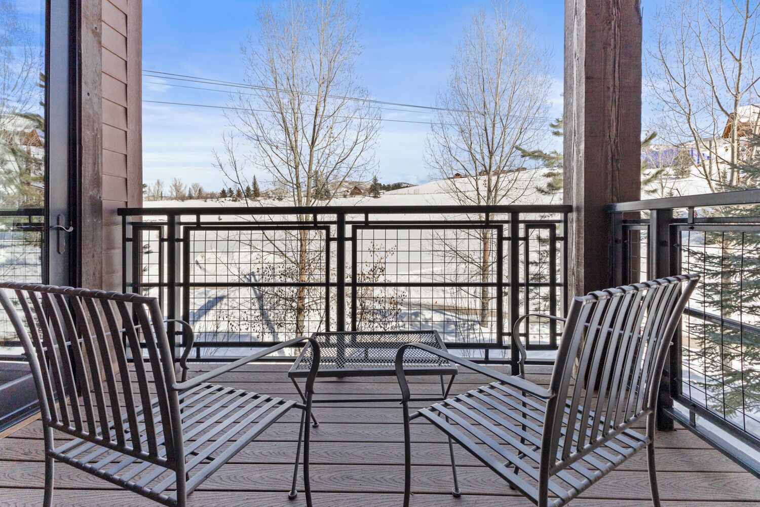 A balcony with metal chairs and a table, overlooking a snowy landscape with bare trees.