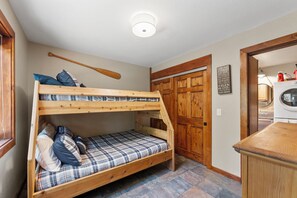 A bunk bed with plaid bedding, a wooden bat, and a wooden door in a room with a tiled floor.