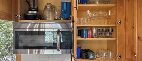 A kitchen with a built-in oven and microwave, a coffee maker, and a cabinet with glassware and cups.
