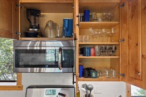 A kitchen with a built-in oven and microwave, a coffee maker, and a cabinet with glassware and cups.