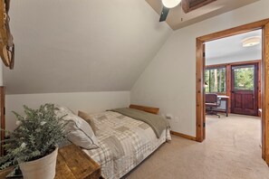 A bedroom with a sloped ceiling, a bed with a quilt, a potted plant, and a view of an outdoor area with a door and a bench.