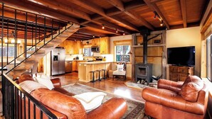 Ein geräumiger Wohnbereich mit Ledersofas, einer Holztreppe, einer Küche und einem Kamin.