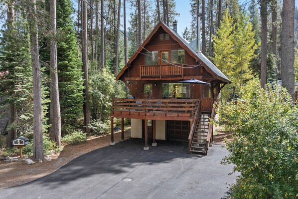 A wooden cabin with a balcony, surrounded by tall trees.