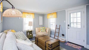 Un salon avec un canapé, une commode en bois, une lampe, un fauteuil et une porte.