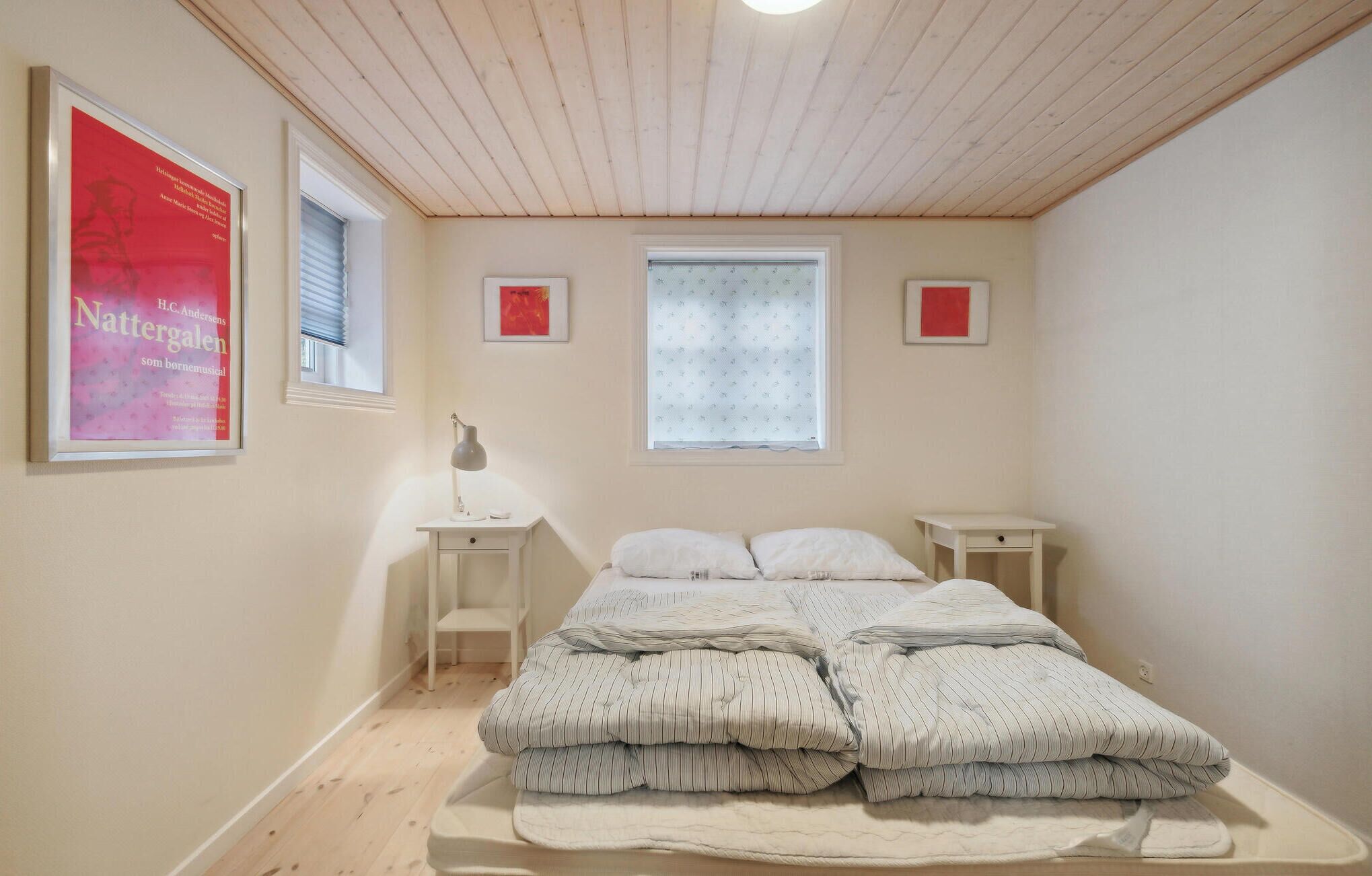 Una camera da letto con soffitto in legno, un letto con lenzuola a righe, due comodini e tre quadri appesi alle pareti.