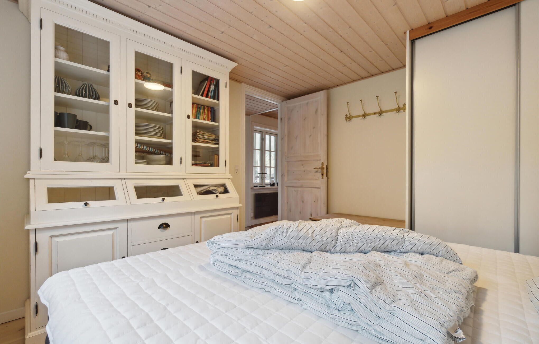A bedroom with a bed, a white wardrobe with glass doors, and a wooden ceiling.