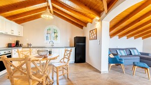 Een moderne keuken met houten balken, een eethoek met houten stoelen, een zwarte koelkast en een grijze bank met blauwe kussens.