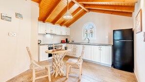 Een keuken met houten balken in het plafond, witte kasten, een zwarte koelkast en een eettafel met stoelen.