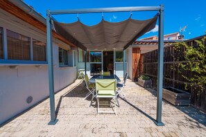 Une terrasse couverte avec une table et des chaises, une clôture en bois et un bâtiment en arrière-plan.