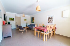 Un espace repas comprenant une table et des chaises, un canapé, un téléviseur et des œuvres d’art accrochées aux murs.